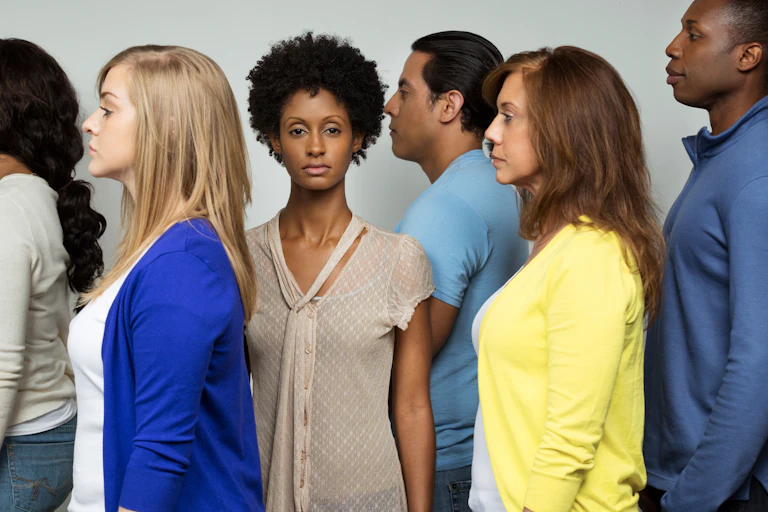 A Black woman looks straight at the camera while people of various ethnicities look to the left.