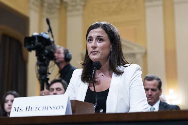 A woman answers a question as she sits behind a desk.