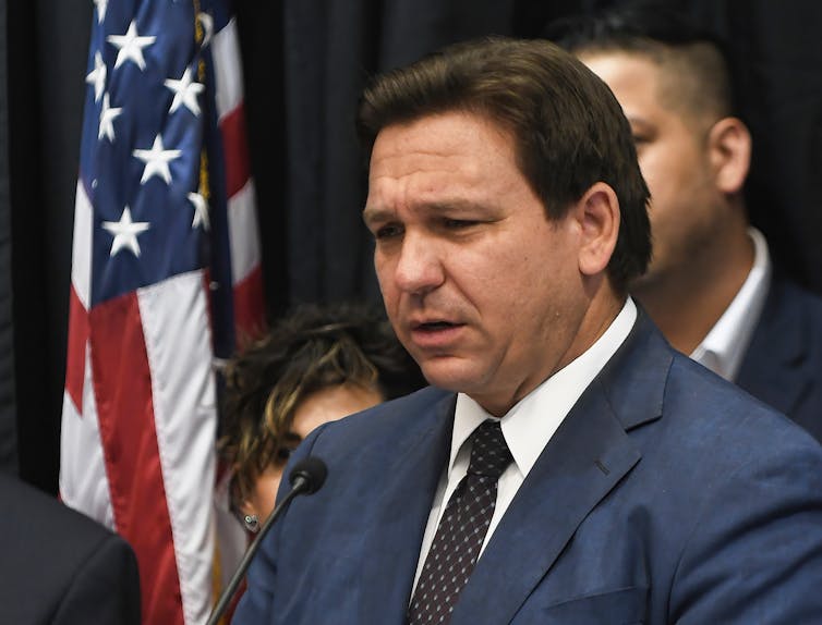 A man wearing a business suit is talking with reporters.