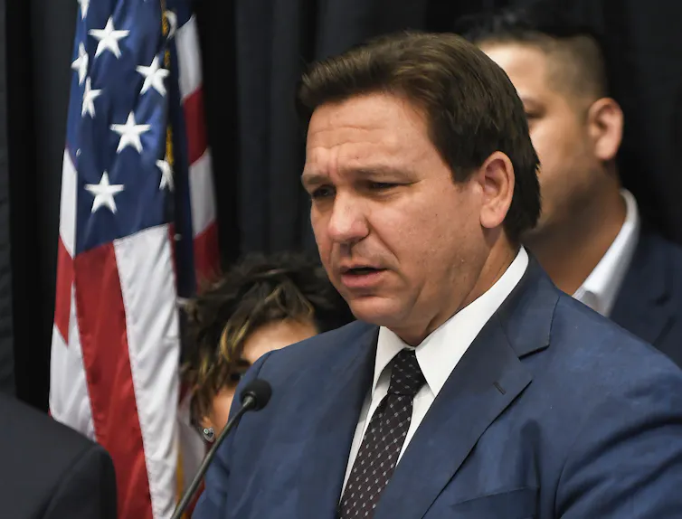 A man wearing a business suit is talking with reporters.