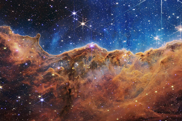 The image is divided horizontally by an undulating line between a cloudscape forming a nebula along the bottom portion and a comparatively clear upper portion. Speckled across both portions is a starfield, showing innumerable stars of many sizes