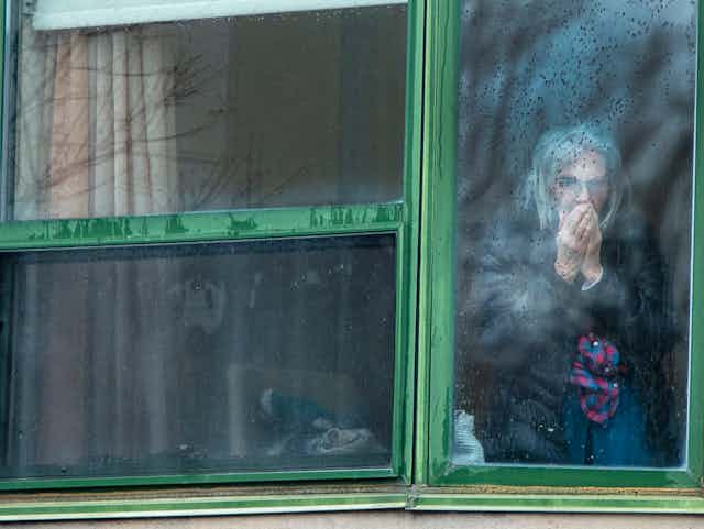an elderly woman stands behind a foggy window