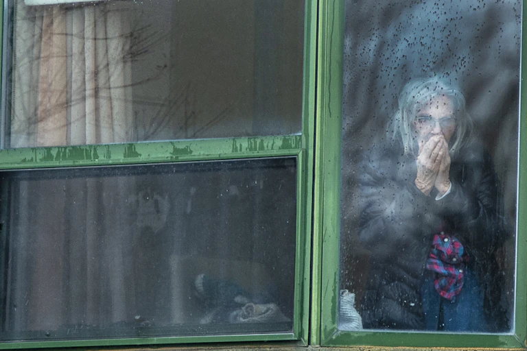an elderly woman stands behind a foggy window