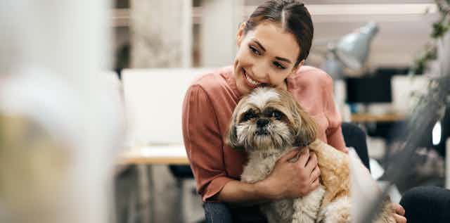 Woman cuddles small dog in office.
