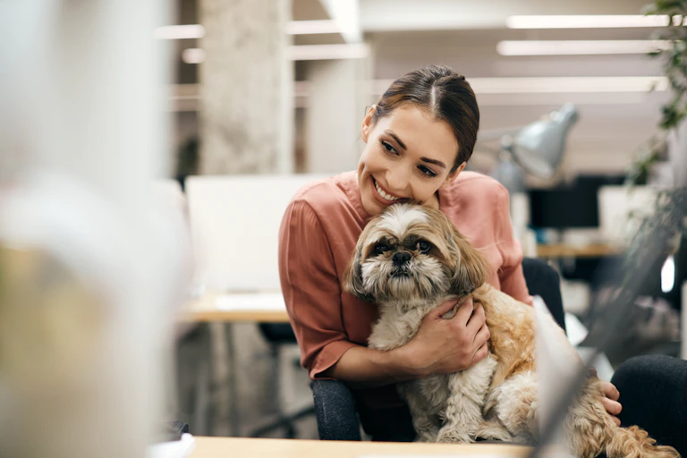 Woman cuddles small dog in office.