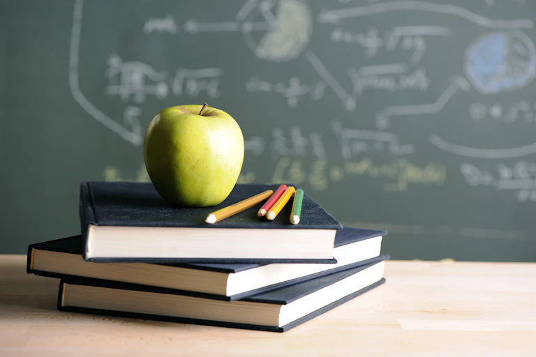 A green apple, on a pile of books in front of a blackboard.