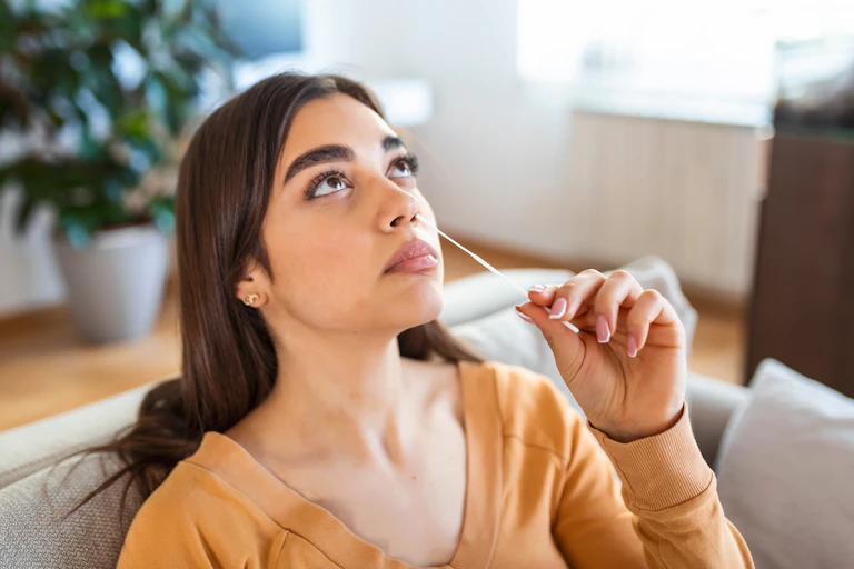 A young woman inserts a swab up her nose.