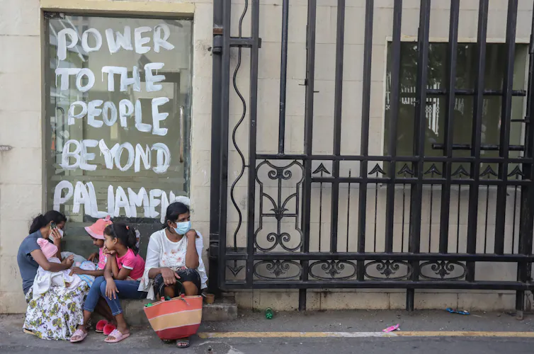 People wait to take a look into the President's palace in Colombo, Sri Lanka, under a sign reading@: Power to the People beyond parliament.