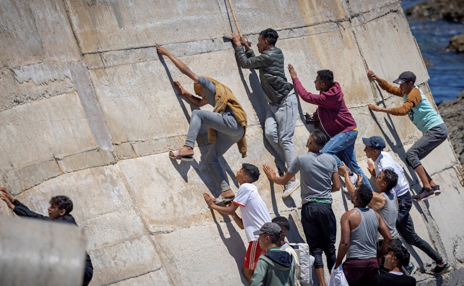 De jeunes migrants tentent de gravir un mur à Fnideq à la frontière maro-espagnole située dans l'enclave de Ceuta, le 21 mai 2021. 