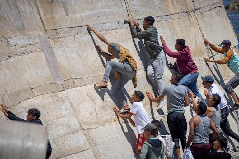De jeunes migrants tentent de gravir un mur à Fnideq à la frontière maro-espagnole située dans l'enclave de Ceuta, le 21 mai 2021.