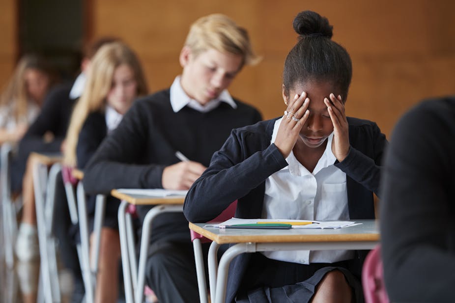 An axious teenage student sitting in a exam school hall with her head in her hands.