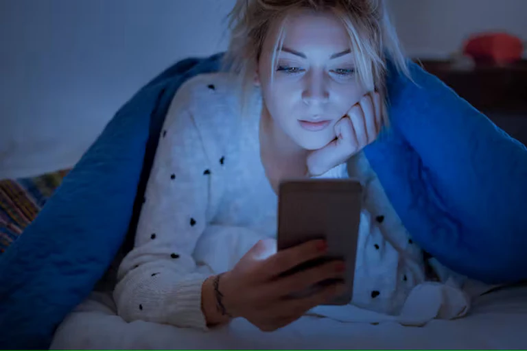 Seorang wanita melihat teleponnya di tempat tidur
