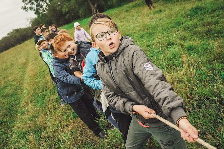 Young boys play tugowar in a green field.