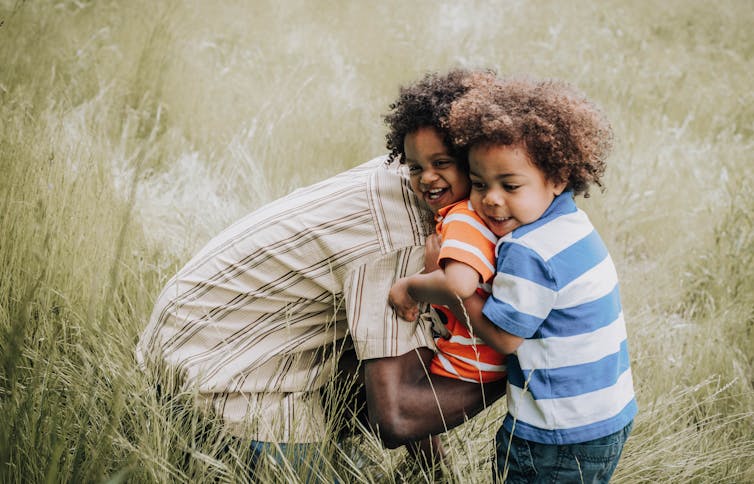 A parent with two young children in a field of long grass.