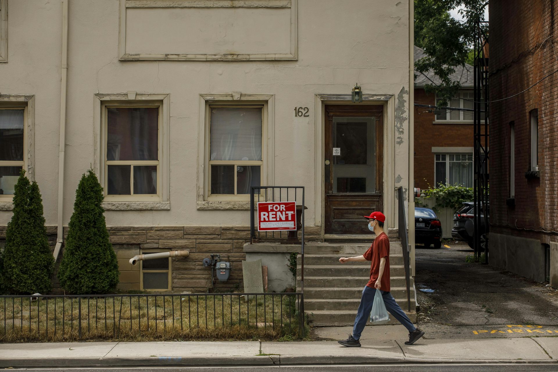 A man walking past a house with a For Rent sign fixed to the porch railing