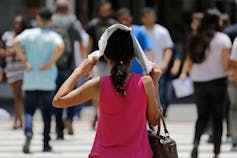 A woman wearing a pink tank talk walking down a street holding a paper over her head to protect from the sun