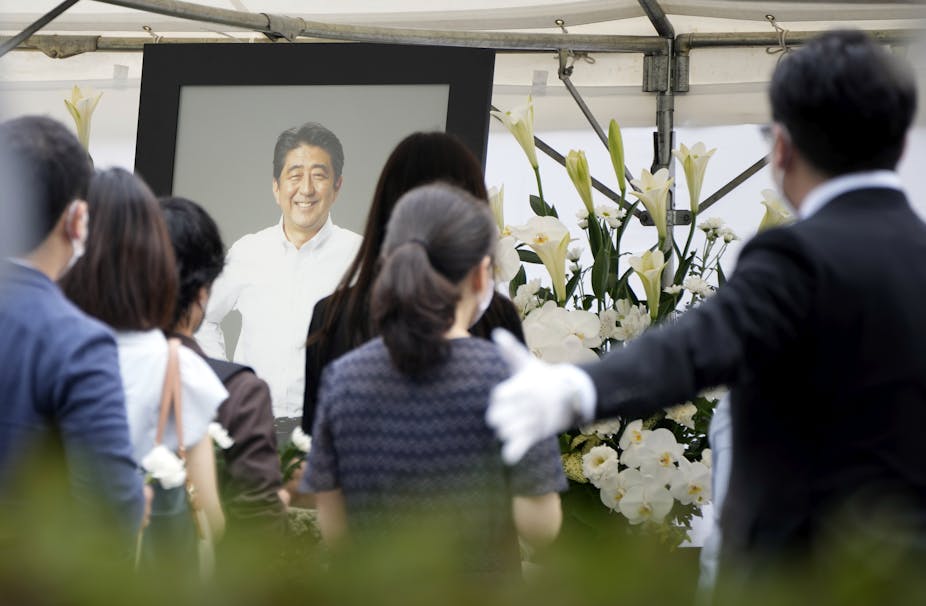 People offering flowers in front of a photograph of Japan's former Prime Minister Shinzo Abe.