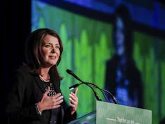 A dark-haired woman smiles as she stands behind a microphone.