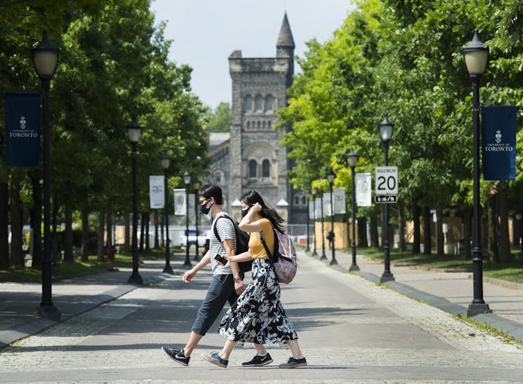 Two students wearing masks walk on a university campus.