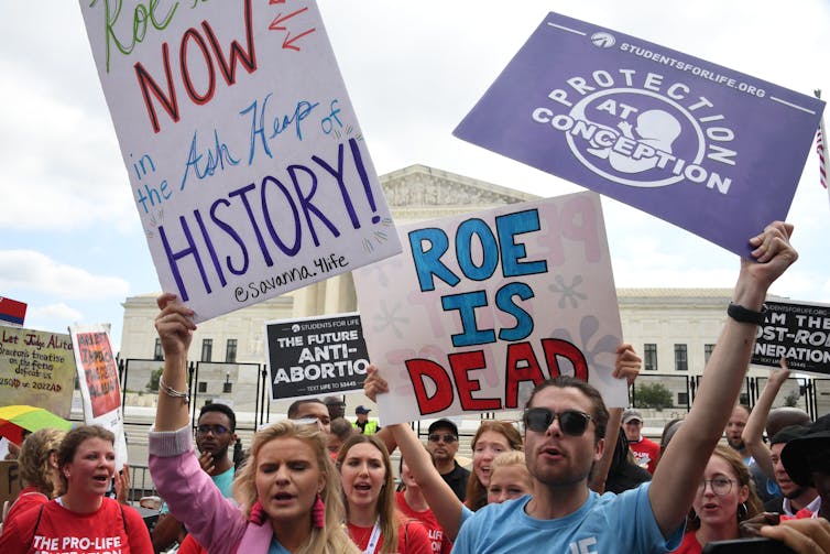 Young white people hold up signs bearing slogans such as 'Roe is dead' outside the Supreme Court building