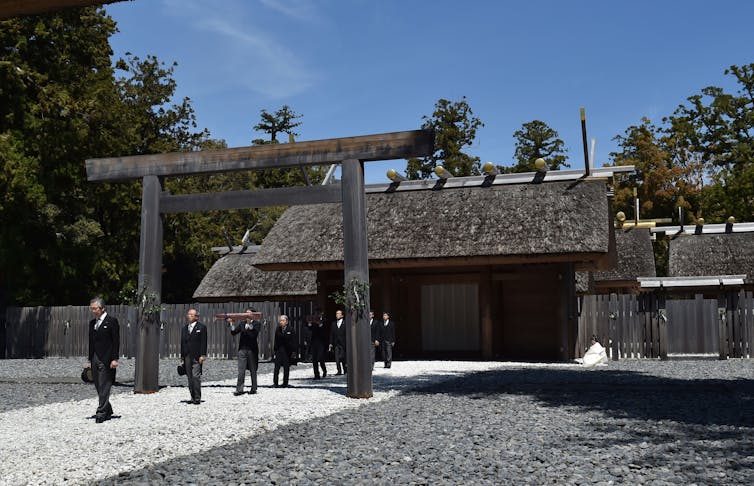 A ritualistic procession showing men dressed in black suits walking in a single line.