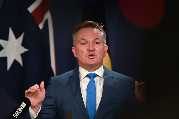 man in suit  speaks in front of flags