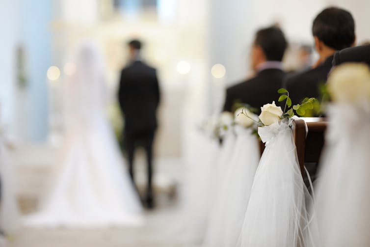 hazy-focus view of back of bride and groom in church with people in pews