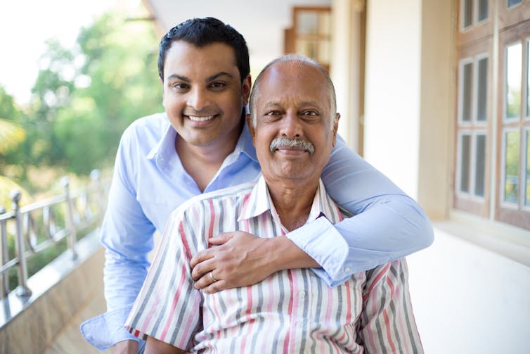 A younger man smiling with his arm around an older man