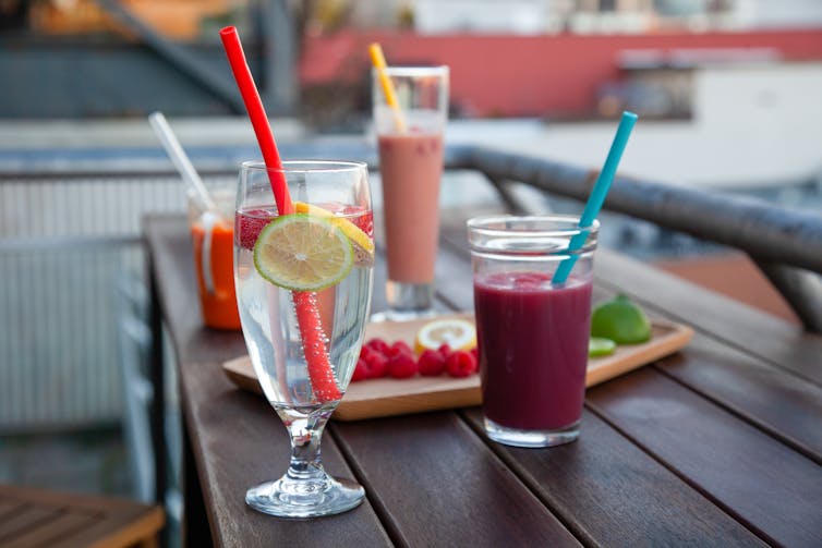 A table with four glasses of juice and some snacks.