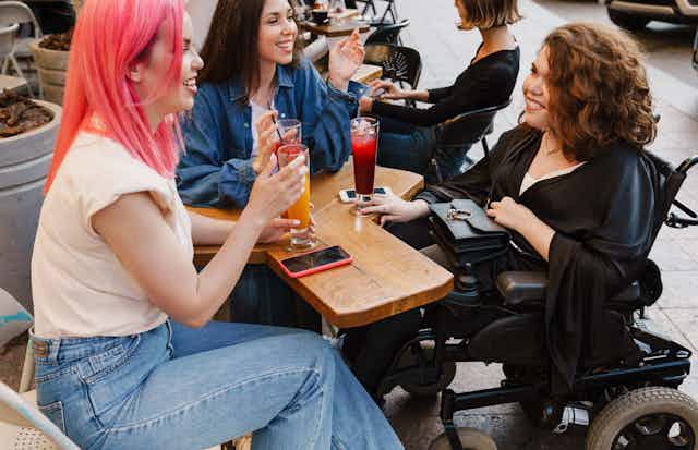 A group of friends sit together grabbing a drink, one is in a wheelchair. They are all using plastic straws