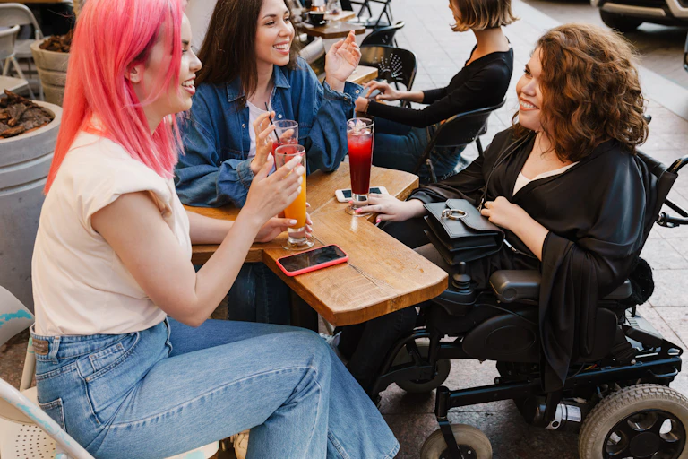 A group of friends sit together grabbing a drink, one is in a wheelchair. They are all using plastic straws