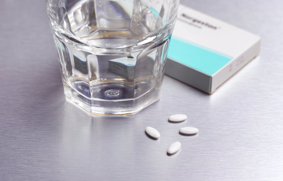 A glass of water, four abortion pills, and a box sit close together on a countertop.