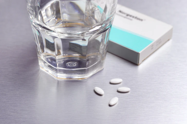 A glass of water, four abortion pills, and a box sit close together on a countertop.