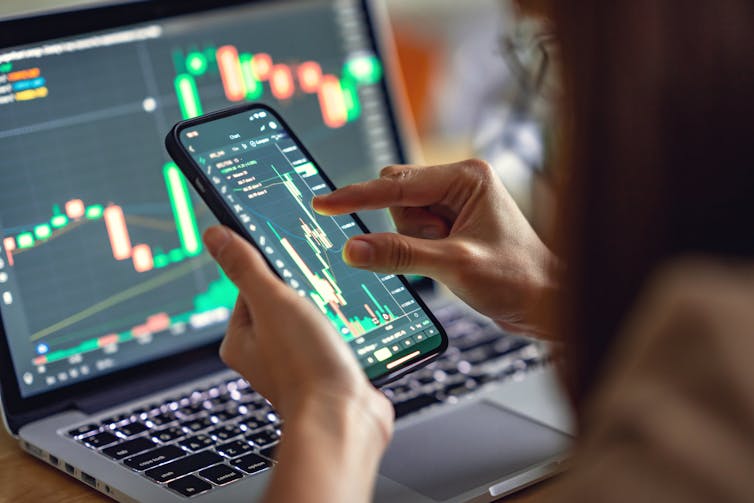 Woman looking at investments on computer and phone screens.