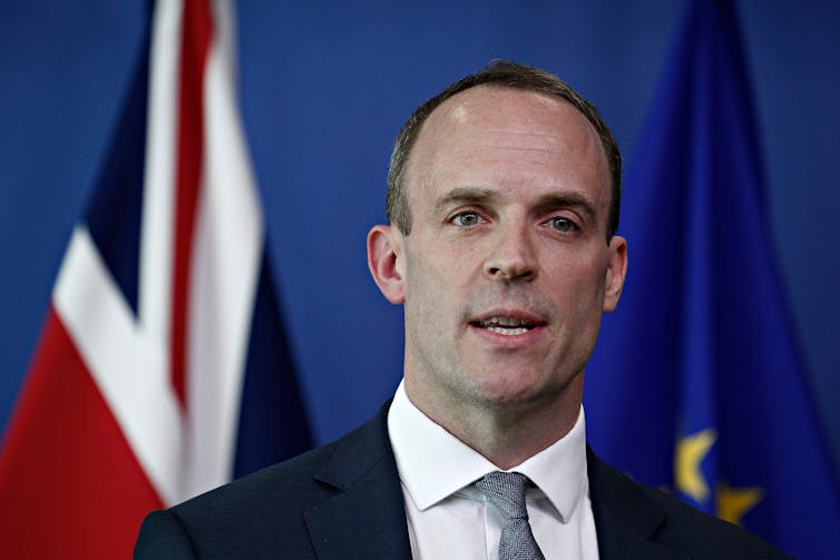 Dominic Raab mid-speech in front of a UK flag and an EU flag