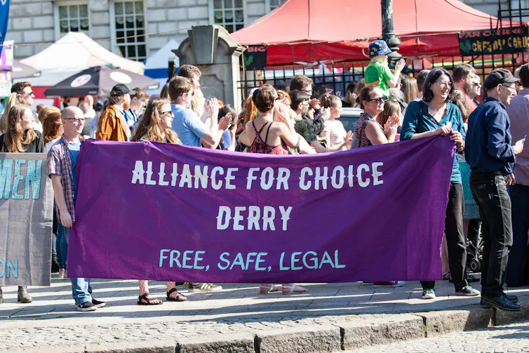Marchers holding a large purple banner reading Alliance For Choice Derry, Free Safe Legal.