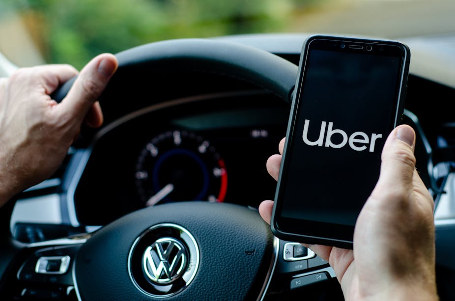 Une main sur un volant de voiture, l'autre main tient un smartphone avec l'application Uber