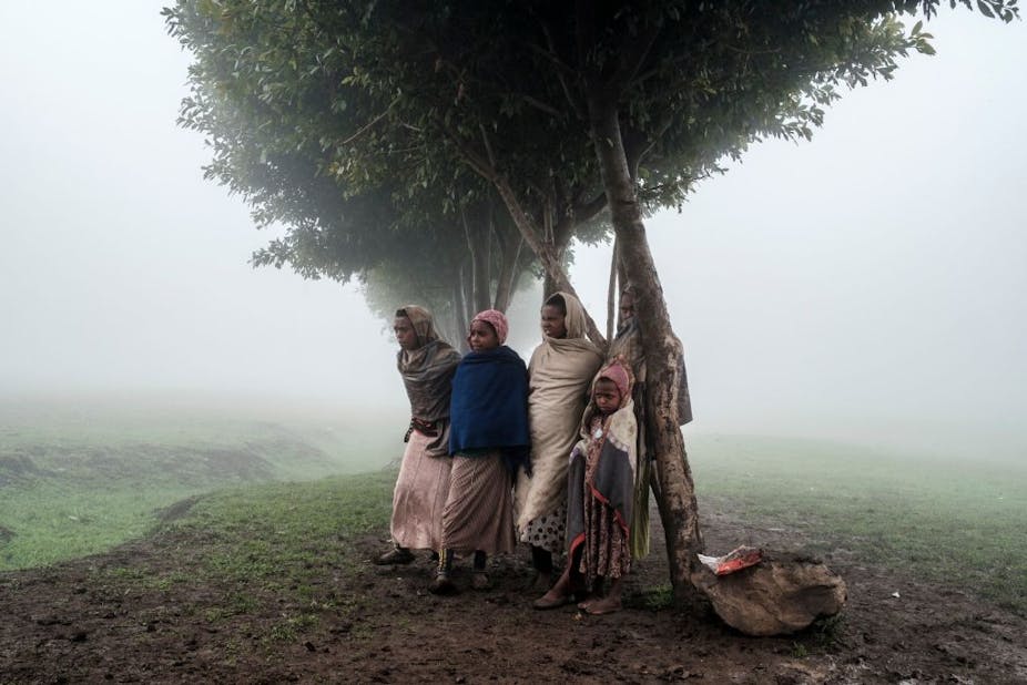 Children stand under a tree in a cold, misty landscape