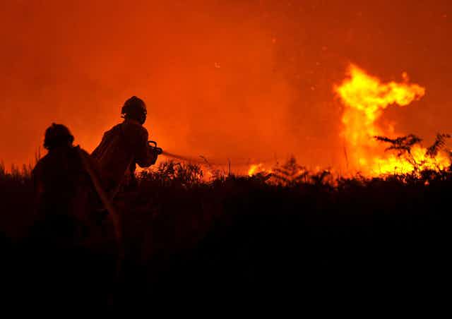 Two firefighters in silhouette battle a wildfire at night.