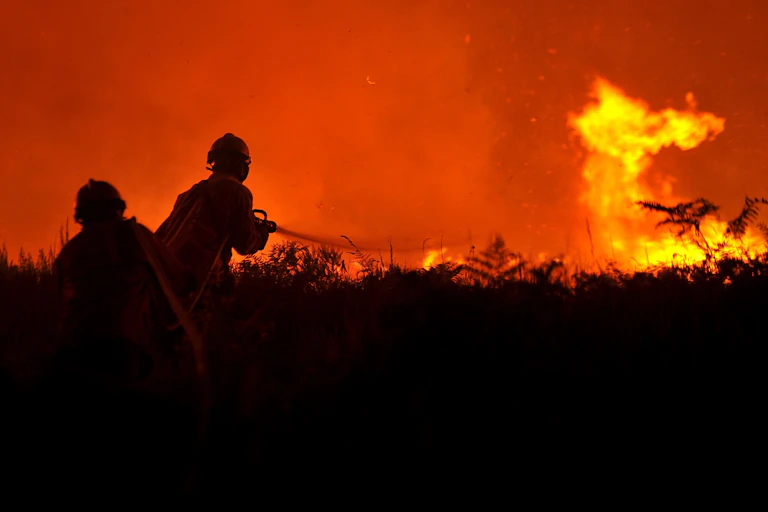 Two firefighters in silhouette battle a wildfire at night.