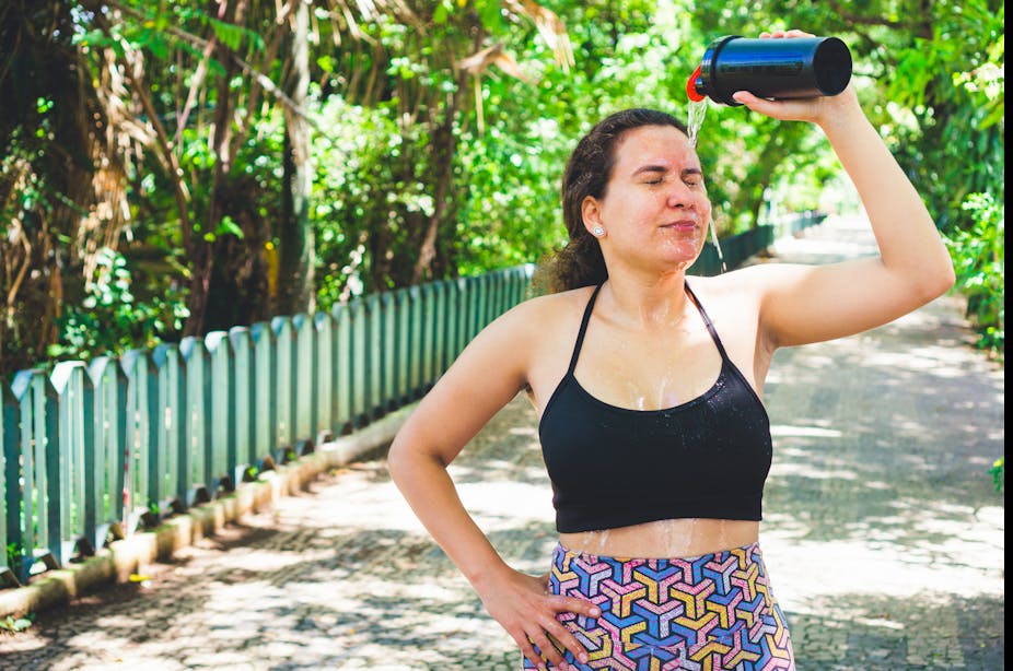 A woman in exercise clothes pours water on her head from a water bottle.