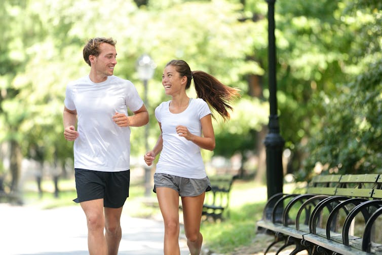 A man and woman go for a run in a park.