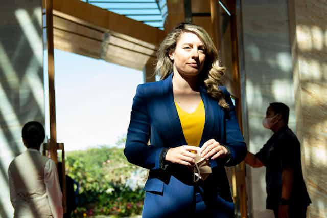 A woman standing wearing a yellow top and a blue blazer