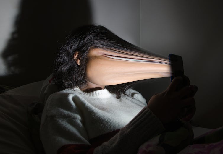 An image of a person lying in bed, holding a smartphone close to their face. The image is highly distorted, with the person’s face elongated and stretched towards the phone, creating a surreal and unsettling effect. The background is dimly lit, and the light from the phone screen casts a glow on the person’s distorted face. The image appears to symbolize the consuming nature of smartphone usage and its impact on the viewer’s perception of space and time.