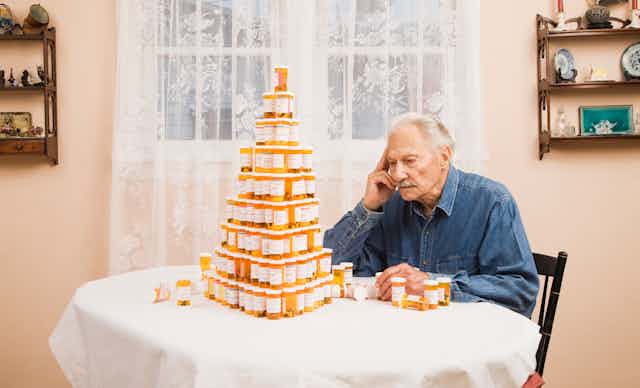 Person sitting at table looking at pyramid of orange pill bottles
