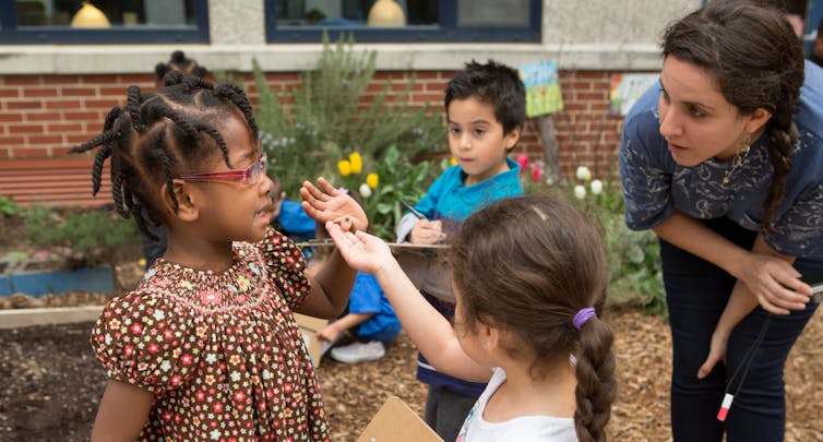 A child holds an insect while talking with a teacher and young children.