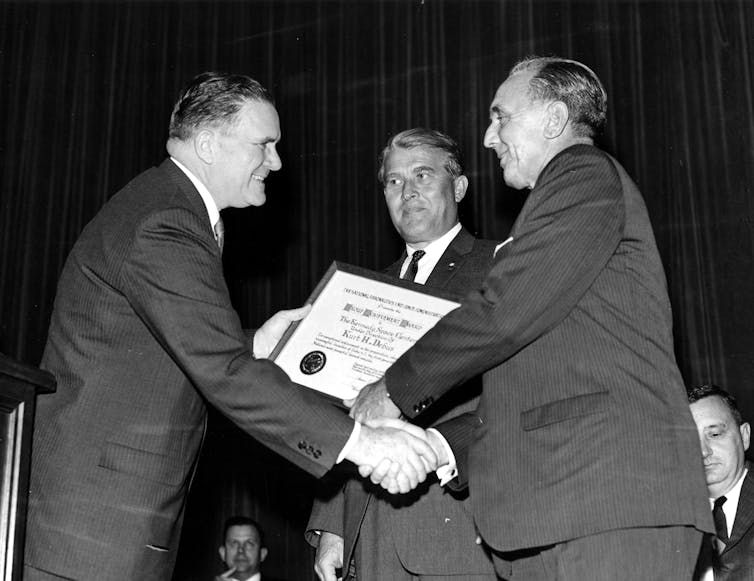 Three men in suits with an award certificate
