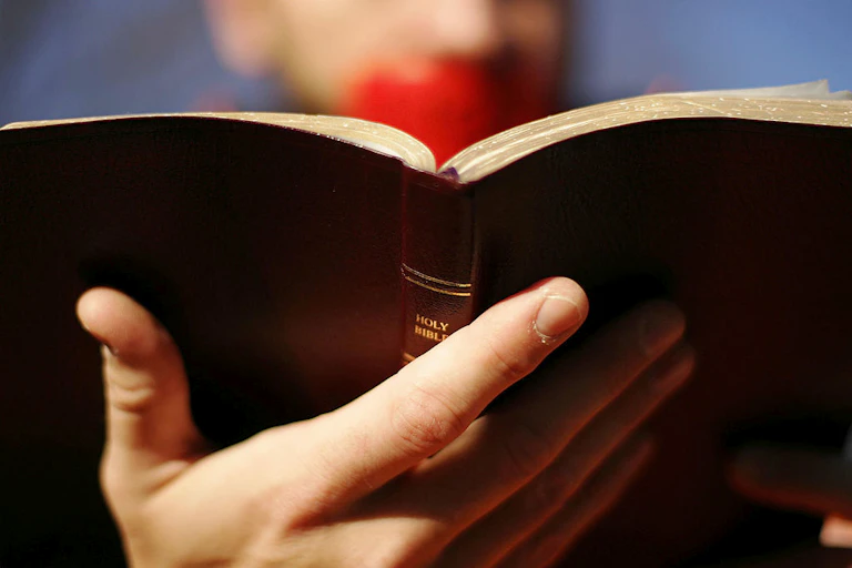 A close-up photo of a Bible held by a person with red duct tape over their mouth.