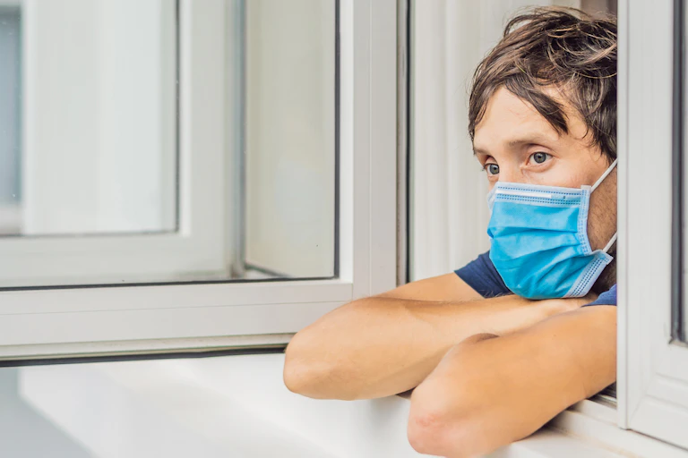 Masked person looking out a window
