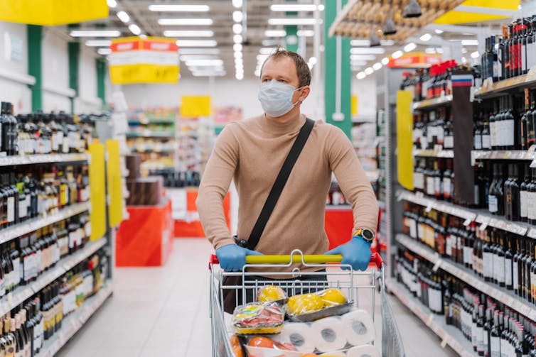 Man with mask pushing supermarket trolly.